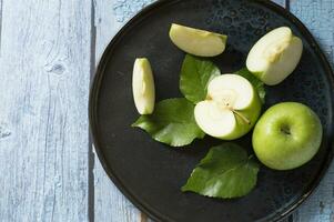 een bord met groen appels en bladeren Aan het foto