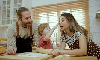 vader en moeder onderwijs baby zoon kneden deeg Aan keuken teller Bij huis. ouders en jongen kind genieten en pret binnenshuis werkzaamheid Koken samen. foto