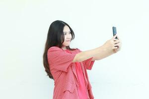 portret van mooi Aziatisch vrouw vervelend rood kleding op zoek Bij mobiel telefoon met gelukkig uitdrukking foto
