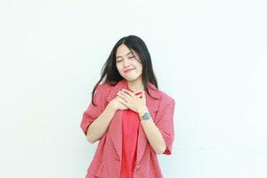 portret van mooi Aziatisch vrouw vervelend rood kleding met hand- gebaren Aan borst terwijl glimlachen foto
