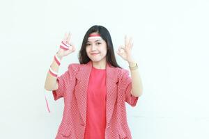 portret van mooi Aziatisch vrouw vervelend rood kleding met mee eens of OK gebaar terwijl glimlachen voor vieren Indonesië onafhankelijkheid dag foto