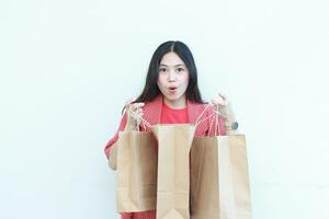 portret van mooi Aziatisch vrouw vervelend rood kleding met verrast gebaar op zoek Bij inhoud van boodschappen doen zak foto