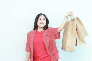 portret van mooi Aziatisch vrouw vervelend rood kleding gebaren draag- veel van boodschappen doen Tassen met gelukkig uitdrukking foto