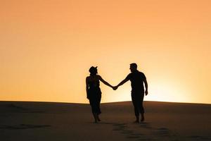 silhouetten van een gelukkig jong koppel op een achtergrond van oranje zonsondergang in de zandwoestijn foto