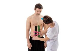 een therapeut plakt heldere kinesiotapes op de maag of buik van een man foto