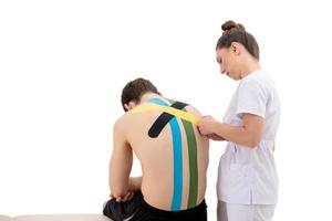 jonge vrouwenfysiotherapeut die speciale fysiotape op de rug van de man toepast foto