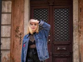 blond modelmeisje met golvend haar in een spijkerjasje staat tegen de achtergrond van een oud gebouw met een vintage deur foto