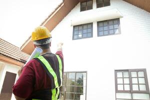 een mannetje ingenieur inspecteert de huis naar leveren het naar de klant. staand in voorkant van de huis, richten naar de voorkant. concept van huis bouw woon- gebouw foto