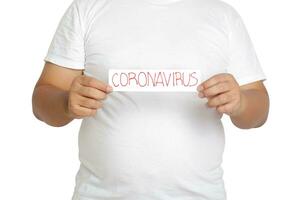 een dik Mens vervelend een wit t-shirt houdt een papier teken geschreven de woorden coronavirus. de concept van Gezondheid zorg voor zwaarlijvig mensen voorkomen virus infectie. knipsel pad. wit achtergrond foto