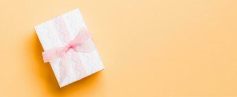 verpakt Kerstmis of andere vakantie handgemaakt Cadeau in papier met roze lint Aan oranje achtergrond. Cadeau doos, decoratie van geschenk Aan gekleurde tafel, top visie met kopiëren ruimte foto