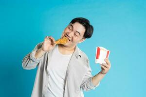 portret van Aziatisch Mens aan het eten snel voedsel Aan blauw achtergrond foto