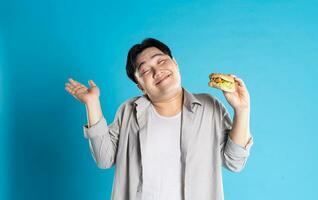 portret van Aziatisch Mens aan het eten snel voedsel Aan blauw achtergrond foto