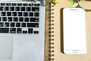 laptop met smartphone Aan notitieboekje, een potlood en bloem pot boom Aan houten achtergrond, boven visie kantoor tafel. foto