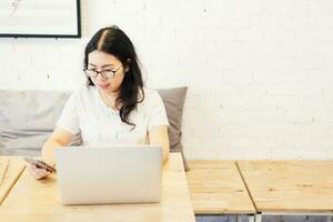 bedrijf Aziatisch vrouw werken met smartphone en laptop computer Aan in koffie winkel Leuk vinden de achtergrond. foto