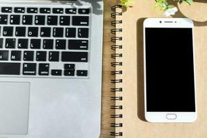 laptop met smartphone Aan notitieboekje, een potlood en bloem pot boom Aan houten achtergrond, boven visie kantoor tafel. foto