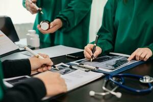 medisch team hebben een vergadering met artsen in wit laboratorium jassen en chirurgisch scrubs gezeten Bij een tafel bespreken een patiënten werken online gebruik makend van computers in de medisch foto