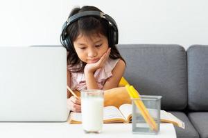 een jong Aziatisch meisje dat computer gebruikt om thuis te leren als protocol voor sociale afstand tijdens covid-19 of coronaviruspandemie. thuisonderwijs concept