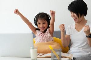 een Aziatische moeder geeft een jonge dochter les van de online computerles als thuisonderwijs vanwege covid-19 of een uitbraak van het coronavirus