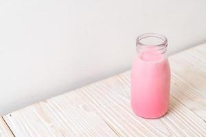 roze melk of aardbeienmelk in fles op hout achtergrond foto