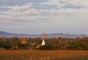 Bagan pagodes velden achter gloden heide met bergachtergrond onder bewolkte blauwe hemel in de ochtend foto