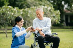 ouderen Aziatisch senior Mens Aan rolstoel met Aziatisch voorzichtig verzorger. verpleging huis ziekenhuis tuin concept zijn wandelen in de tuin. naar helpen en aanmoedigen. foto