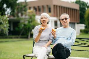 Aziatisch senior paar hebben een mooi zo tijd. ze lachend en glimlachen terwijl zittend buitenshuis Bij de park. lief senior paar foto