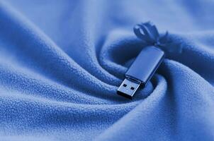 USB flash geheugen kaart met boog leugens Aan een deken van zacht en harig fleece kleding stof met een veel van Verlichting vouwen. fantoom klassiek blauw kleur foto