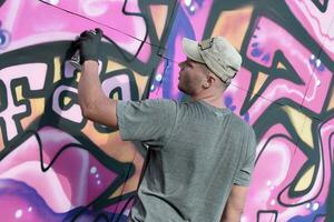 jong Kaukasisch mannetje graffiti artiest tekening groot straat kunst schilderij in blauw en roze tonen foto