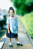 portret van een gelukkig klein meisje in een thais schooluniform dat op het voetpad staat, klaar om terug naar school te gaan foto