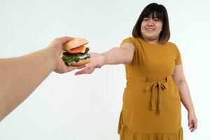 hongerig te zwaar jong Aziatisch vrouw Holding Hamburger Aan geïsoleerd achtergrond, haar hongerig allemaal tijd en te veel eten, gulzigheid en eetbui aan het eten. haar levensstijl is aan het eten snel voedsel allemaal tijd. ongezond concept foto