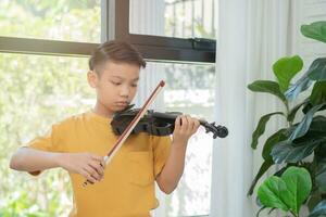 een klein Aziatisch kind speelt en oefent viool muzikaal snaarinstrument tegen in huis, concept van muzikaal onderwijs, inspiratie, tiener kunstacademie student. foto