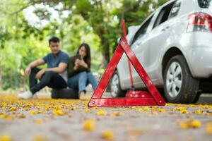 Aziatisch paar gebruik makend van smartphone voor bijstand na een auto afbreken Aan straat. concept van voertuig motor probleem of ongeluk en noodgeval helpen van professioneel monteur foto