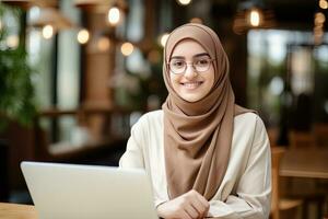 portret van mooi moslim vrouw leerling online aan het leren in koffie winkel, jong vrouw met hijab studies met laptop in cafe, meisje aan het doen haar huiswerk foto