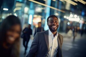 portret van gelukkig Afrikaanse Amerikaans zakenman wandelen Aan straat Bij nacht, glimlachen zwart manager in modern stad omringd door wazig mensen. foto