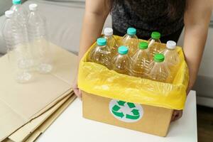 huis recycle eco groen nul concept vrouw het werpen leeg plastic fles in recycling bak met geel vuilnis Tassen Bij huis. foto