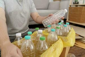 huis recycle eco groen nul concept Mens het werpen leeg plastic fles in recycling bak met geel vuilnis Tassen Bij huis foto