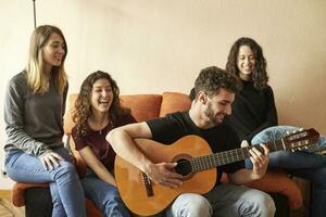 gelukkig vrienden luisteren naar Mens spelen gitaar Aan bankstel foto