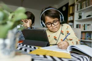 jongen schrijven aantekeningen door digitaal tablet zittend met mannetje vriend gedurende e-learning Bij huis foto