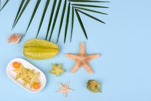 fruitcarambol, strandaccessoires en gebladerte van een tropische plant op gekleurd papier foto