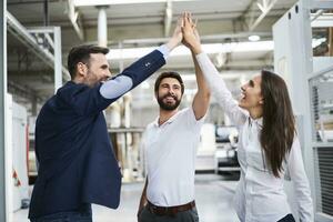 gelukkig zakenman en medewerkers hoog vijf in een fabriek foto