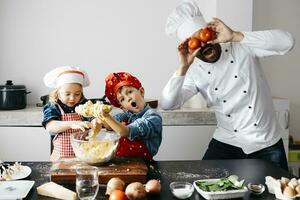 speels vader met twee kinderen aan het bedekken zijn ogen met tomaten in keuken foto