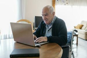 portret van inhoud senior Mens in rolstoel gebruik makend van laptop Bij huis foto