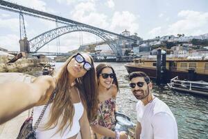 vrolijk jong vrienden nemen selfie tegen douro rivier- in stad, porto, Portugal foto