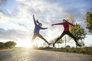 jong Dames hebben pret en jumping in park, tegen ochtend- zon foto