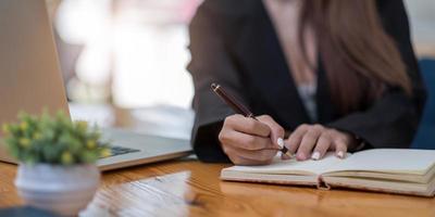 close-up van de handen van de vrouw met een laptop, een notebook en een pen die aantekeningen maakt foto