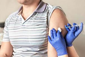 een arts vaccineert een man tegen het coronavirus in een kliniek. detailopname. het concept van vaccinatie, immunisatie, preventie tegen covid-19.