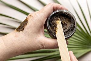 in de hand van een vrouw zit een pot met een bodyscrub gemaakt van natuurlijke ingrediënten. handgemaakte cosmetica. thuis kuuroord. foto