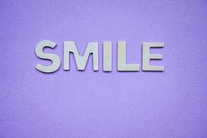 glimlach woord met houten letters op de paarse achtergrond foto