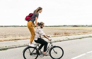 gelukkig jong paar rijden samen Aan een fiets Aan land weg foto
