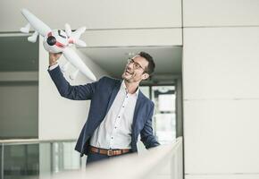 lachend zakenman spelen met speelgoed- vliegtuig in kantoor gebouw foto